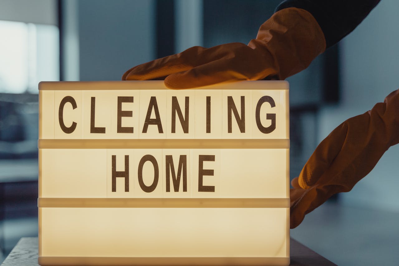 Latex-gloved hands holding a lightbox sign with CLEANING HOME text.